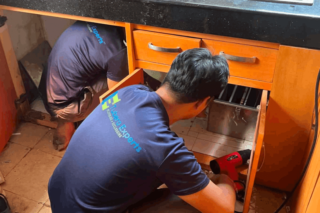 Tubero Experts plumbers installing a grease trap under a kitchen sink.