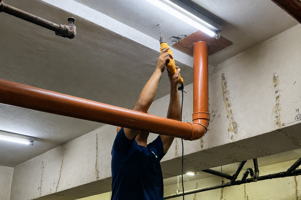 Tubero Experts plumber drilling into a ceiling to mount new sanitary line piping during leak repair.