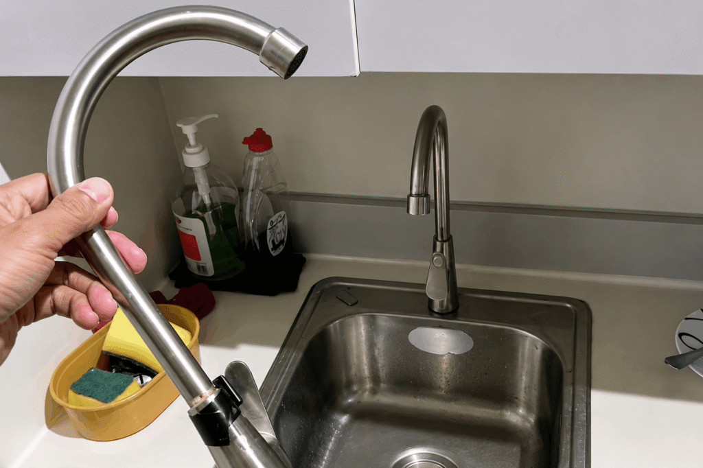 Hand adjusting a newly installed pull-down kitchen faucet over a stainless steel sink