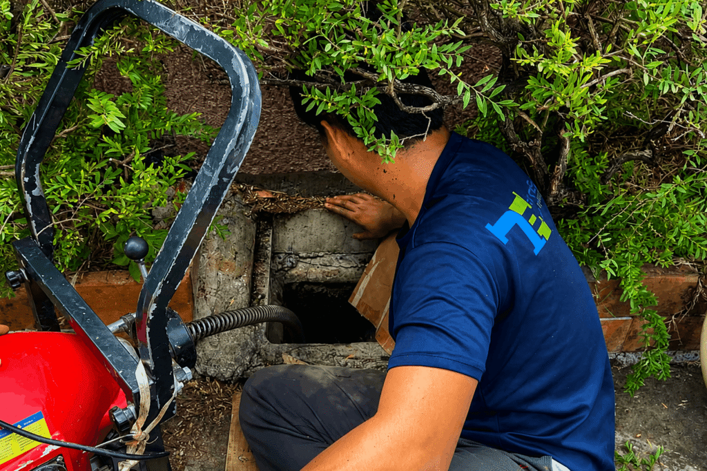 Tubero Experts plumber performing drain declogging service using a motorized drain machine on a blocked outdoor drain