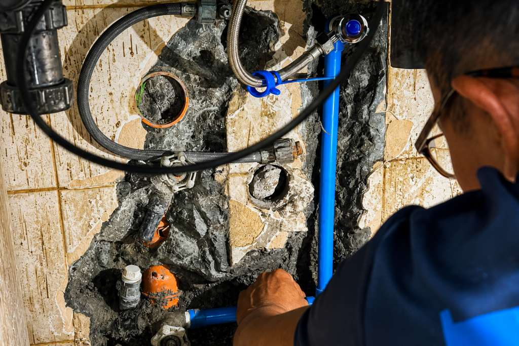 Tubero Experts plumber inspecting exposed water line pipes and connections behind bathroom tiles.