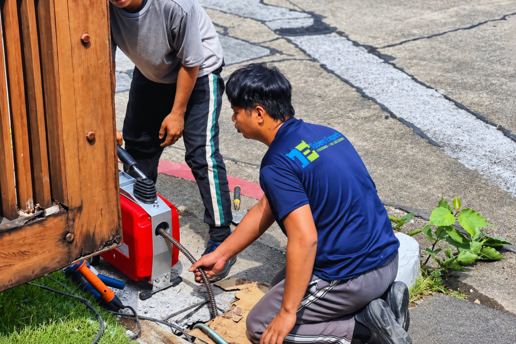 Tubero Experts technician in uniform operating a drain declogging machine on a residential property