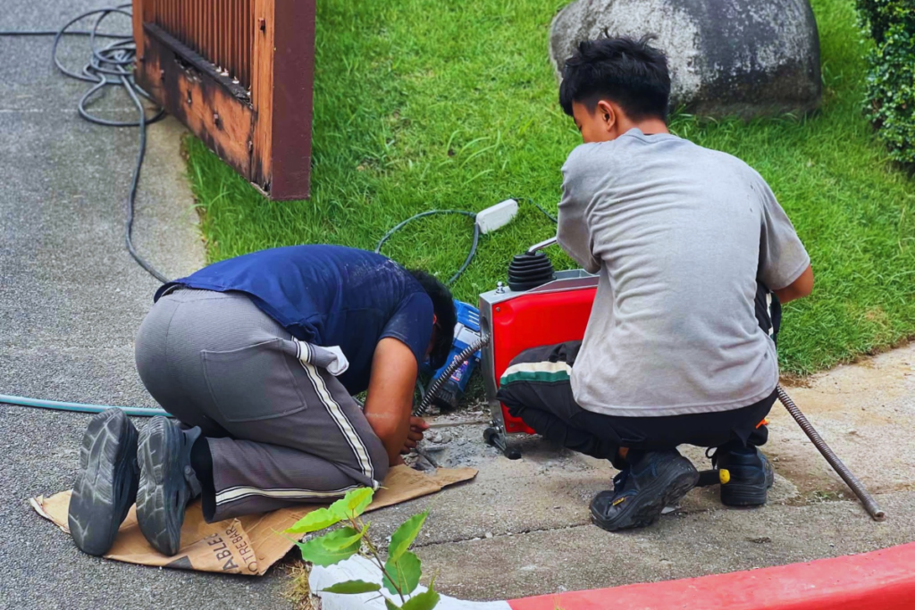 Two plumbing technicians using a drain cleaning machine on a driveway drain