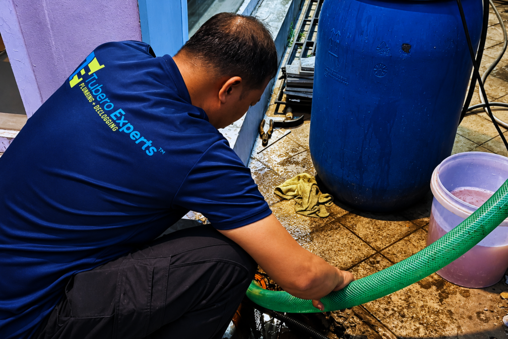 Tubero Experts technician draining a blocked outdoor drain with a green hose