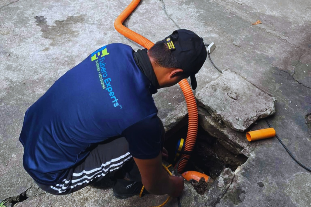 Tubero Experts technician cleaning an open drain pit with a hose
