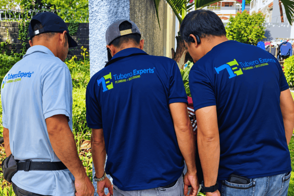 Three Tubero Experts plumbers inspecting a problem area outside a home