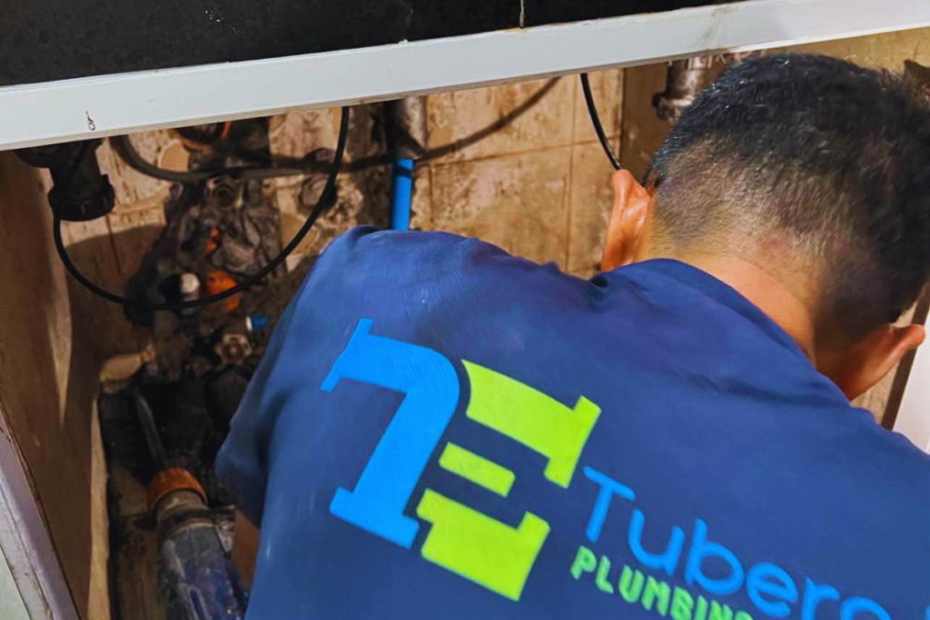 Tubero Experts technician repairing exposed pipes inside a bathroom wall