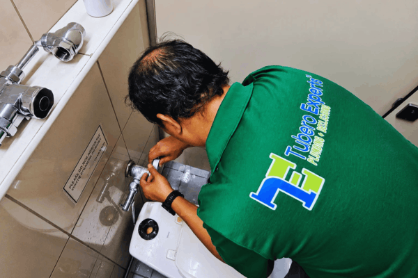 Tubero Experts plumber fixing a wall-mounted flush valve in a restroom