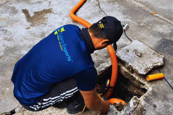 Tubero Experts plumber working inside an open drain access hole with a flexible hose