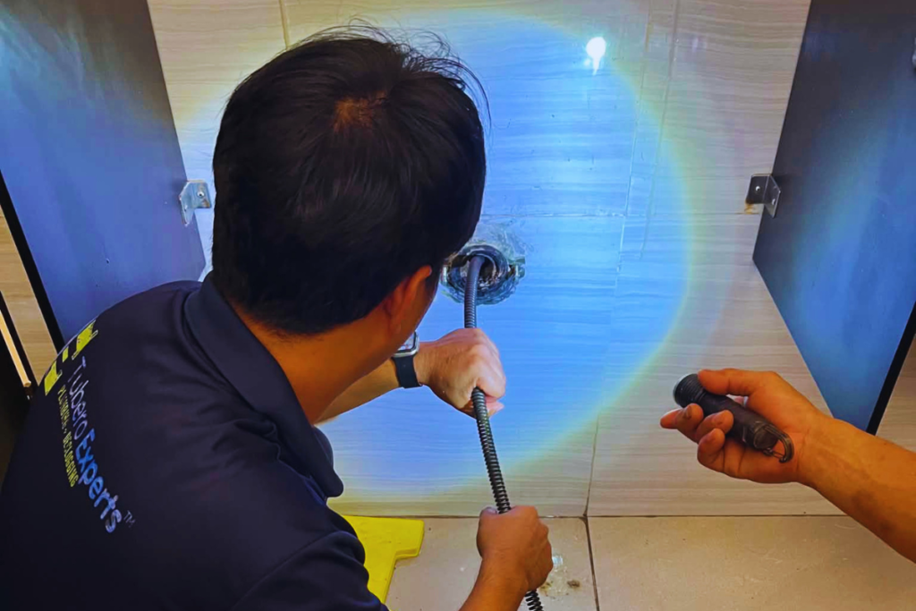 Technician feeding a drain cable into a restroom floor drain