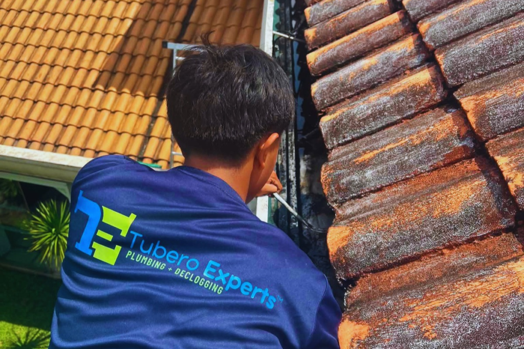 Tubero Experts technician inspecting a roof gutter beside weathered clay roof tiles
