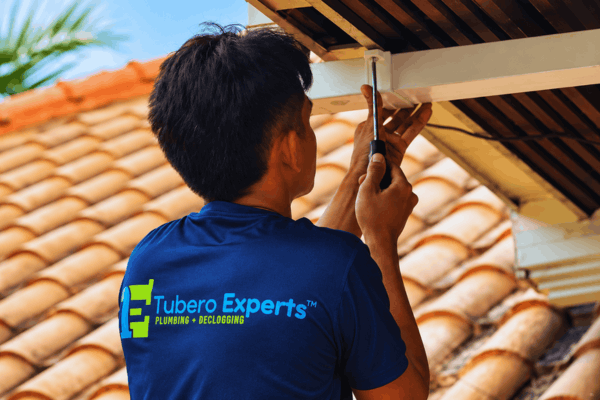 Plumber tightening a screw on a wooden beam under a clay tile roof overhang