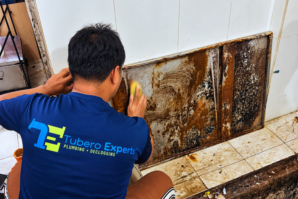 Tubero Experts technician scrubbing a greasy grease trap cover in a kitchen