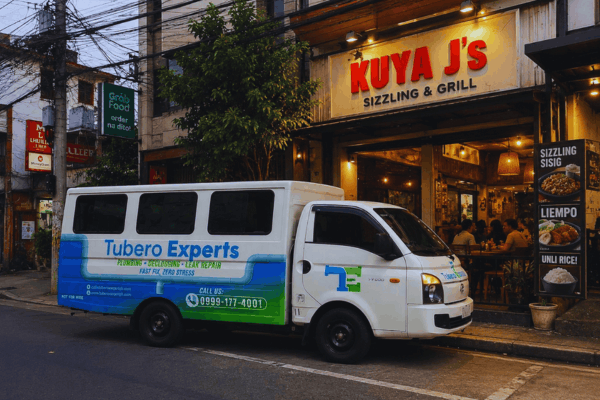 Tubero Experts van parked on a busy city street in front of a lit-up grill restaurant at dusk