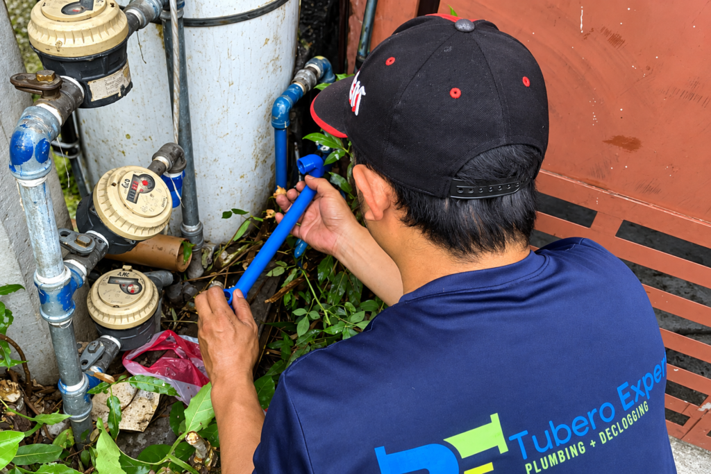 Tubero Experts plumber fitting a blue pipe beside water meters
